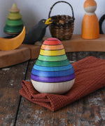 Mader wooden rainbow roly-poly wobbly pear toy placed on a cloth on a wooden surface in the Babipur playroom.