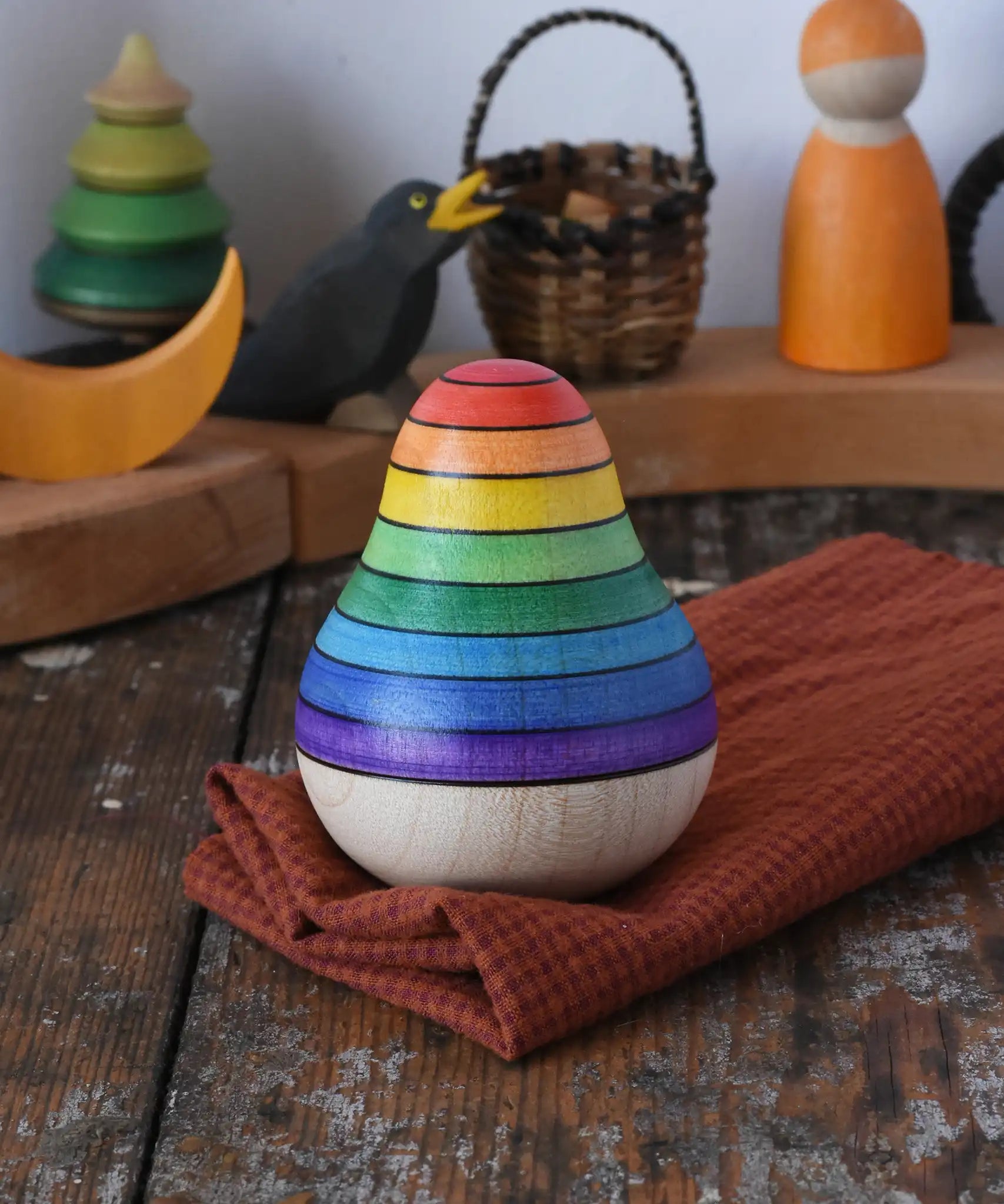 Mader wooden rainbow roly-poly wobbly pear toy placed on a cloth on a wooden surface in the Babipur playroom.