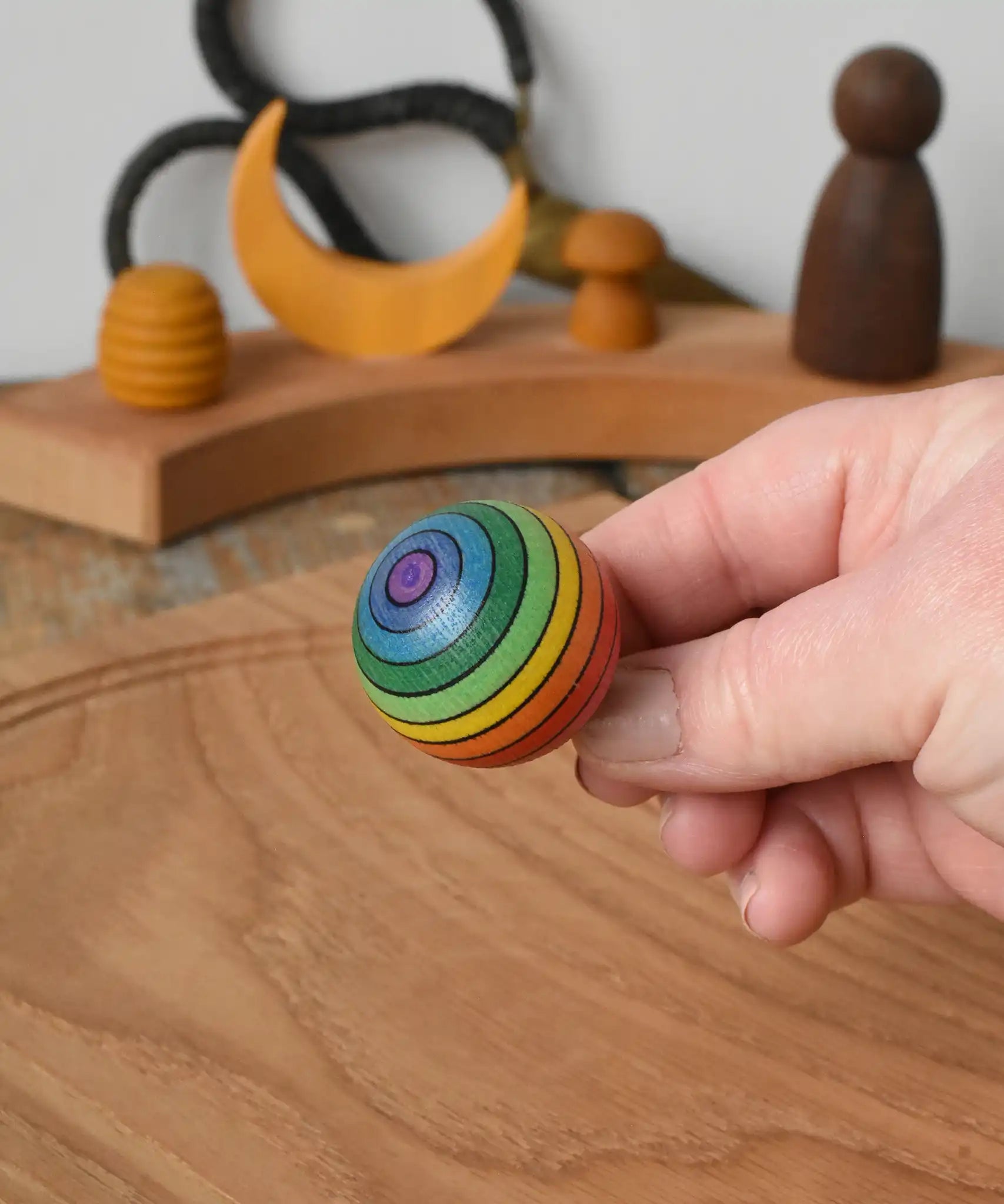 Mader Kreiselmanufaktur rainbow spinning turn-over top in an adult's hand in the Babipur playroom.