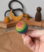 Mader Kreiselmanufaktur rainbow spinning turn-over top in an adult's hand in the Babipur playroom.