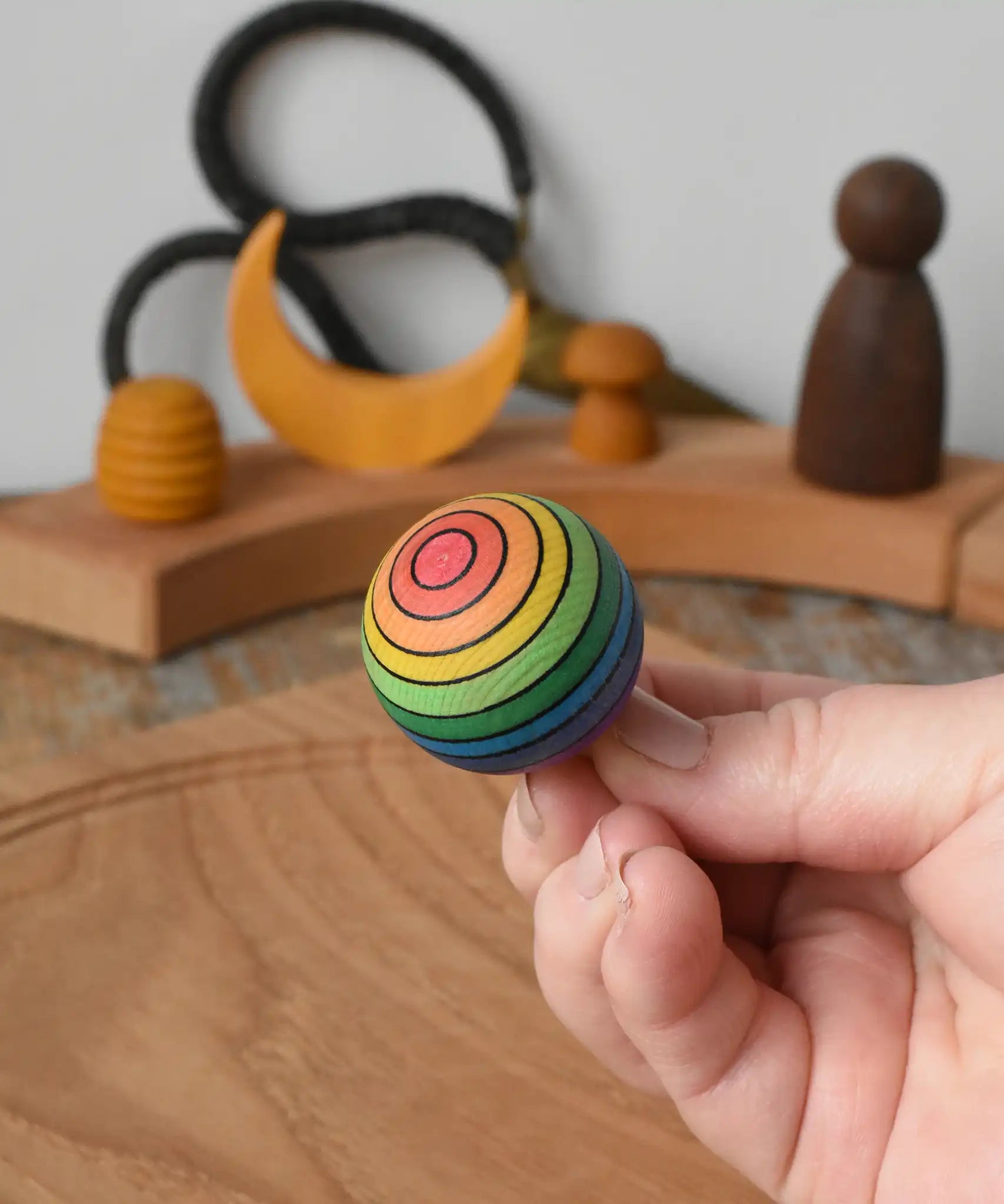 Mader Kreiselmanufaktur rainbow spinning turn-over top in an adult's hand in the Babipur playroom.