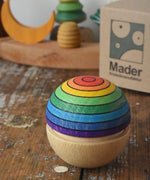 Mader Kreiselmanufaktur rainbow wobble placed on a wooden desk in the Babipur playroom. The cardboard packaging box can be seen in the background along with a decorated Grimm's celebration ring. 