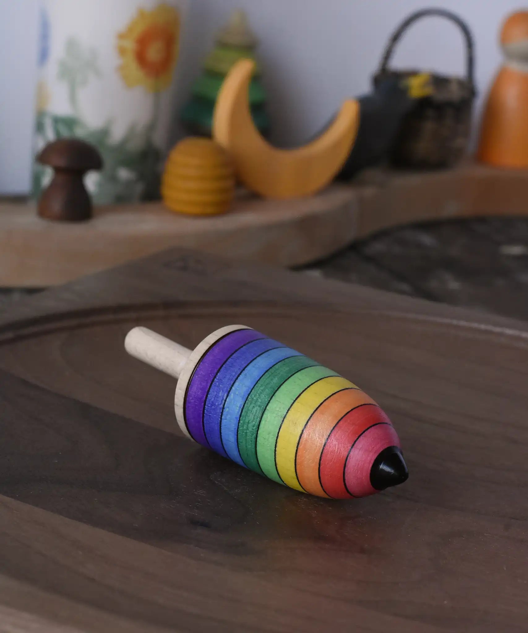 Mader rainbow stripe wooden spinning top placed on a walnut wood plate in the Babipur playroom. 
