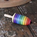 Mader rainbow stripe wooden spinning top placed on a wooden desk in the Babipur playroom. 