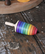 Mader rainbow stripe wooden spinning top placed on a wooden desk in the Babipur playroom. 