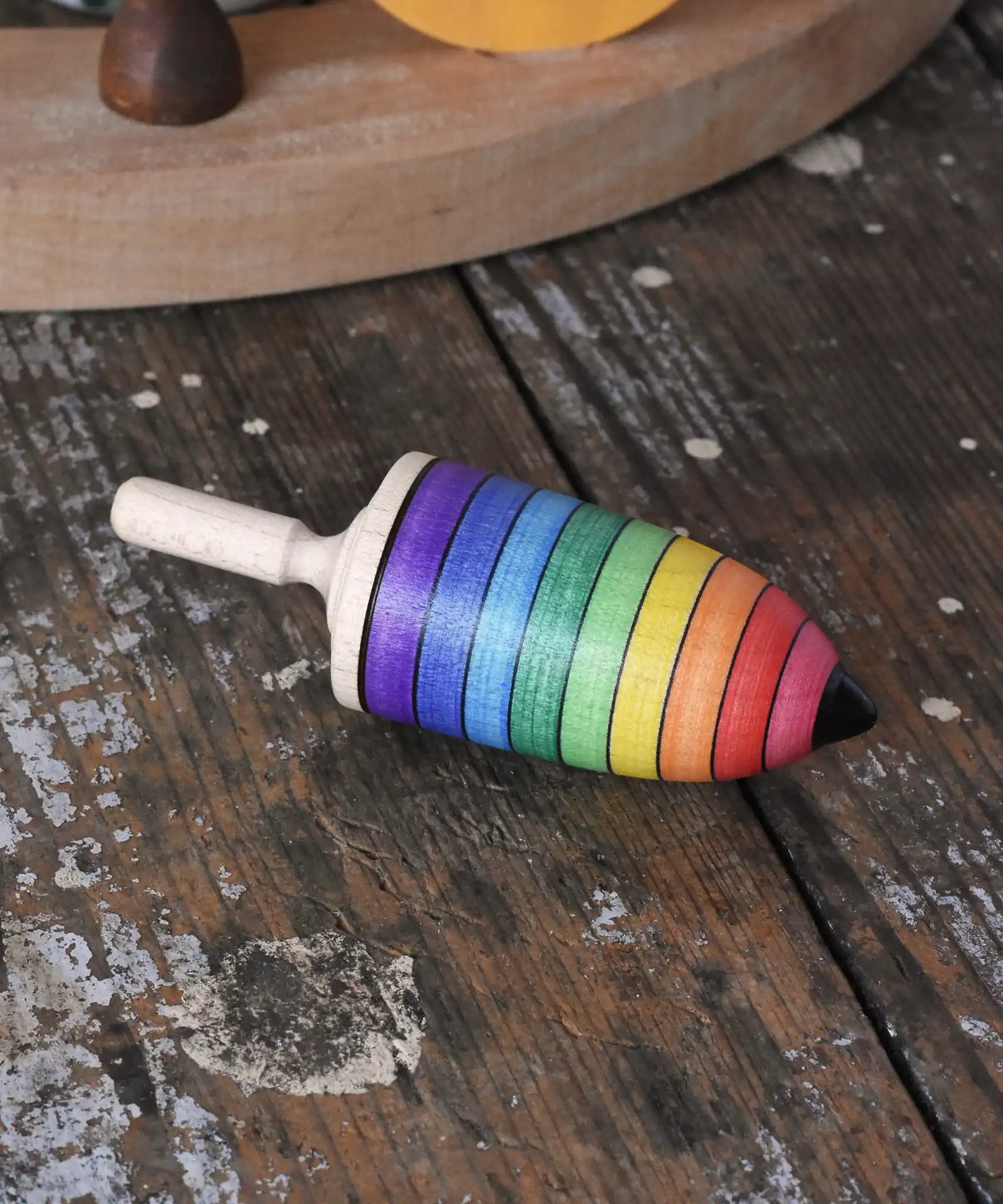Mader rainbow stripe wooden spinning top placed on a wooden desk in the Babipur playroom. 