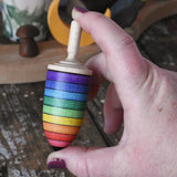 Mader rainbow stripe wooden spinning top placed in an adult's hand.