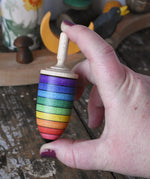 Mader rainbow stripe wooden spinning top placed in an adult's hand.