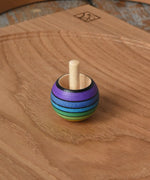 Mader Kreiselmanufaktur rainbow spinning turn-over top placed on an oak spinning plate on a wooden desk in the Babipur playroom.