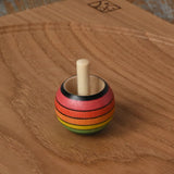 Mader Kreiselmanufaktur rainbow spinning turn-over top placed on an oak spinning plate on a wooden desk in the Babipur playroom.