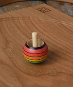 Mader Kreiselmanufaktur rainbow spinning turn-over top placed on an oak spinning plate on a wooden desk in the Babipur playroom.