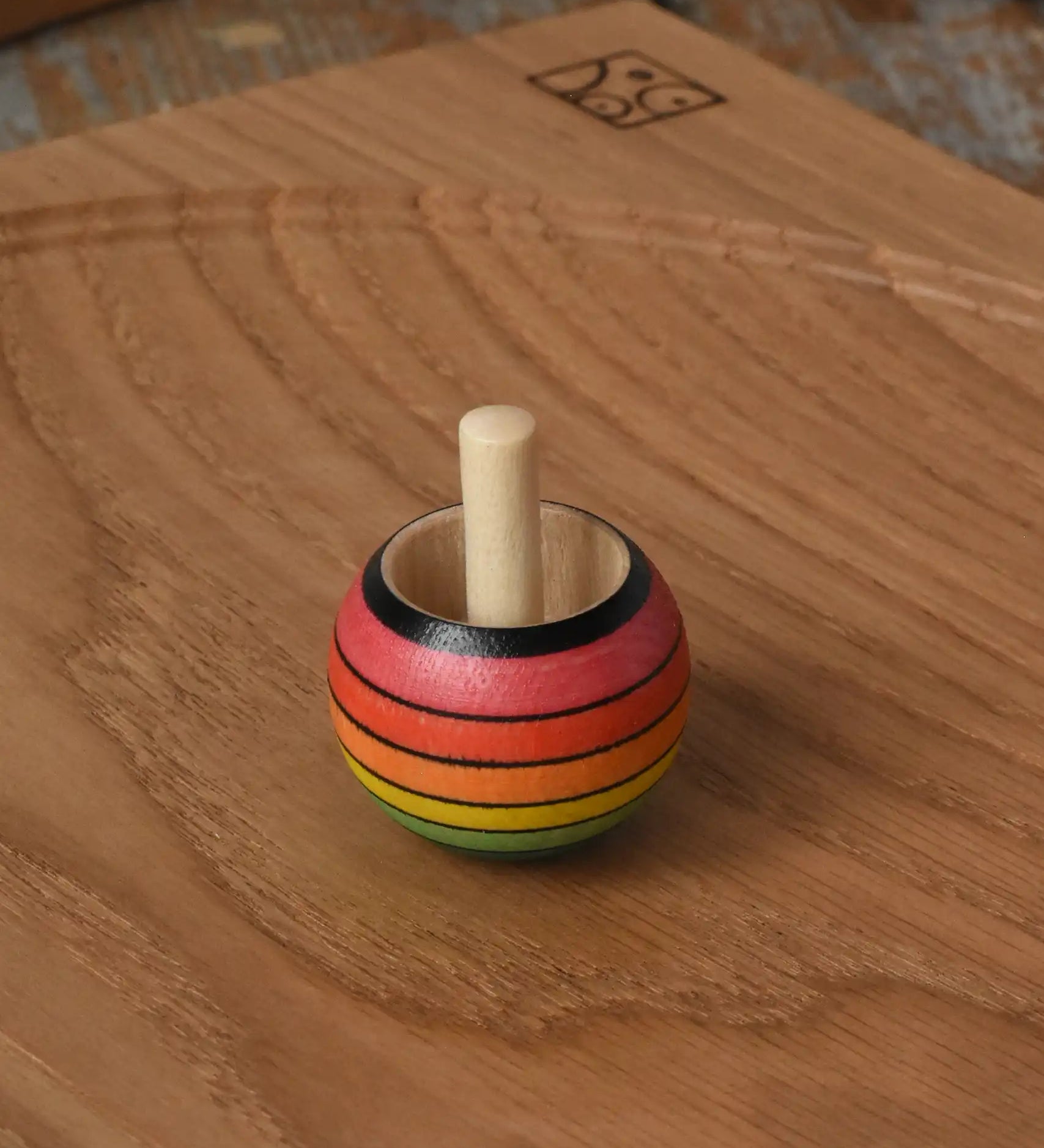 Mader Kreiselmanufaktur rainbow spinning turn-over top placed on an oak spinning plate on a wooden desk in the Babipur playroom.