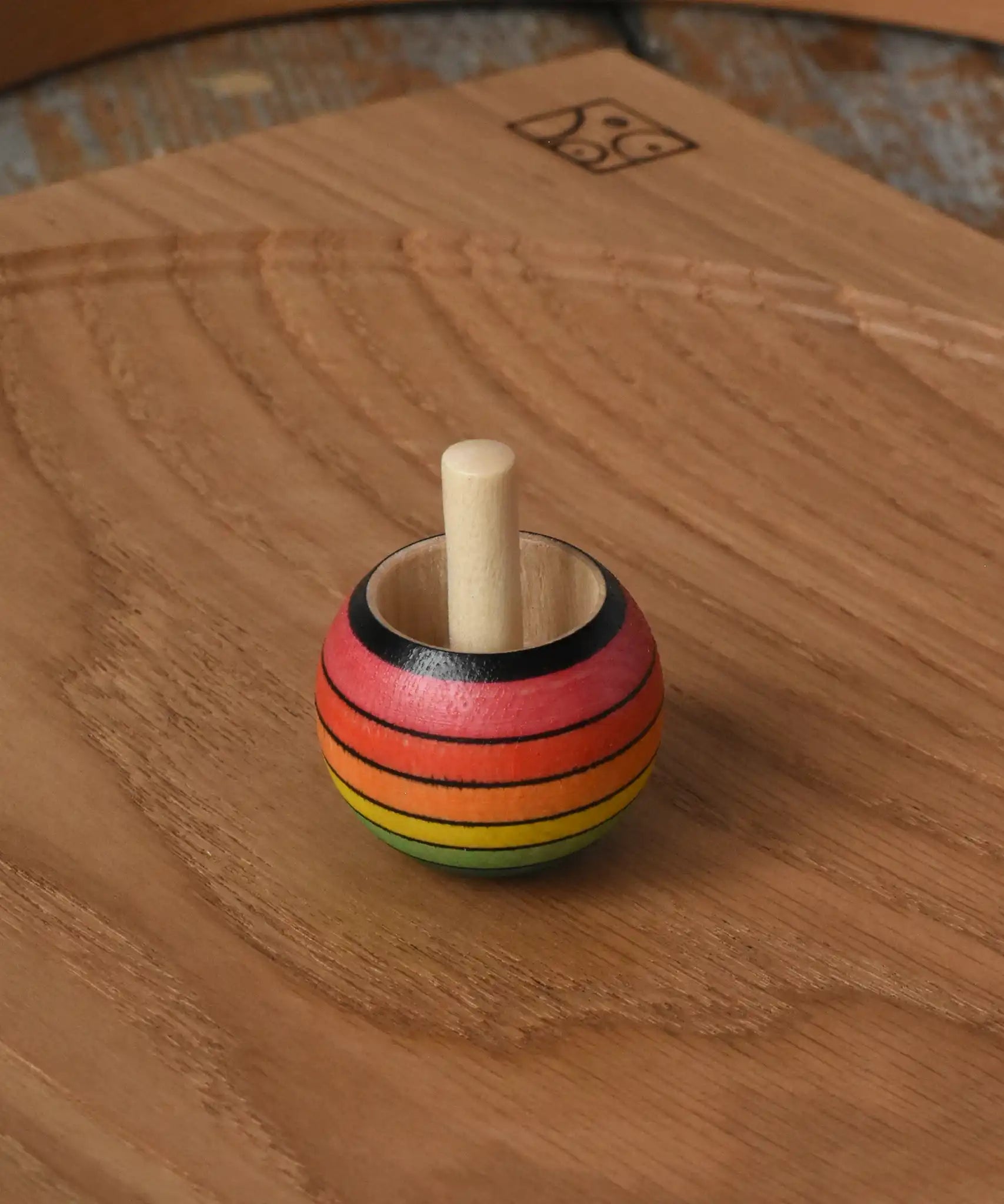 Mader Kreiselmanufaktur rainbow spinning turn-over top placed on an oak spinning plate on a wooden desk in the Babipur playroom.