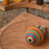 Bottom of the Mader Kreiselmanufaktur ring pull string spinning top placed on a cherry wood spinning plate in the Babipur playroom.
