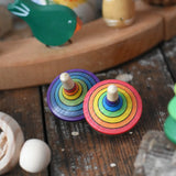 Two rainbow rallye style traditional striped rainbow spinning top toys placed on a wooden desk in the Babipur playroom.