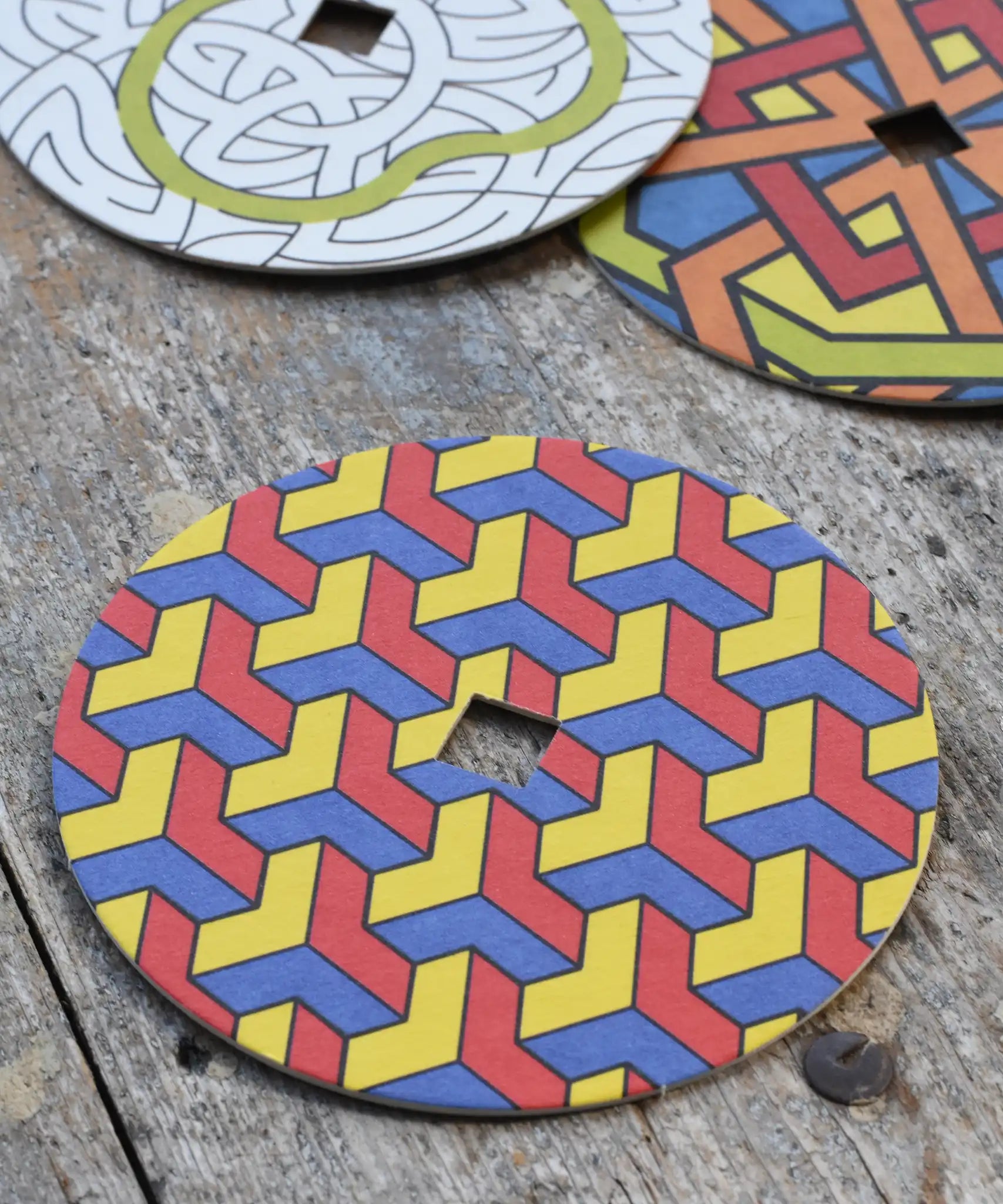 Mader patterned and coloured cardboard discs for 'So And So' Spinning Top placed on a wooden surface in the Babipur playroom. 