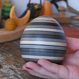 Mader Kreiselmanufaktur roly-poly wooden egg in graphite in an adult's hand in the Babipur playroom.
