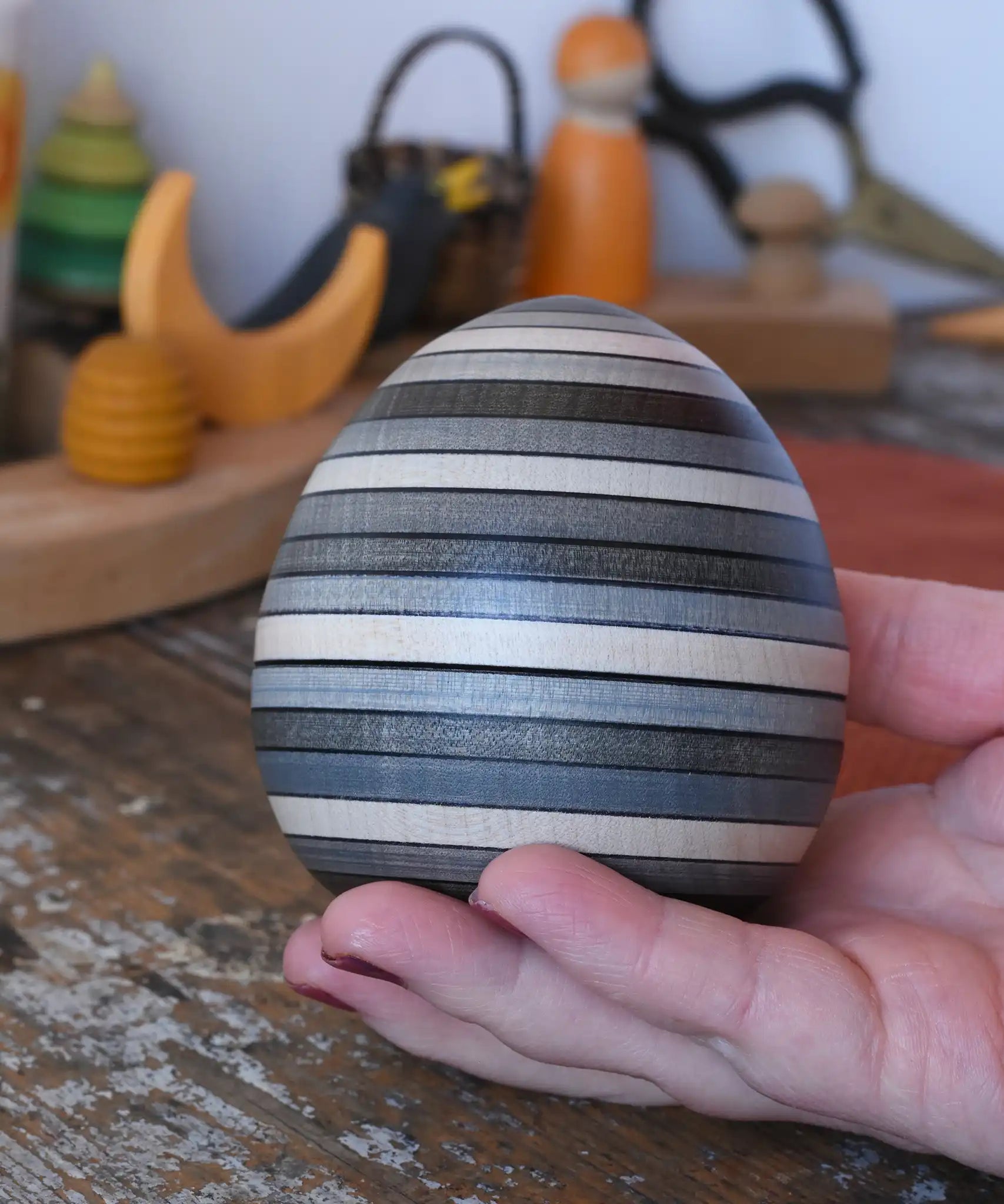 Mader Kreiselmanufaktur roly-poly wooden egg in graphite in an adult's hand in the Babipur playroom.