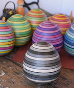 Mader Kreiselmanufaktur roly-poly wooden egg in graphite placed on a wooden surface in the Babipur playroom. Other colour ways of the egg can be seen in the background. 