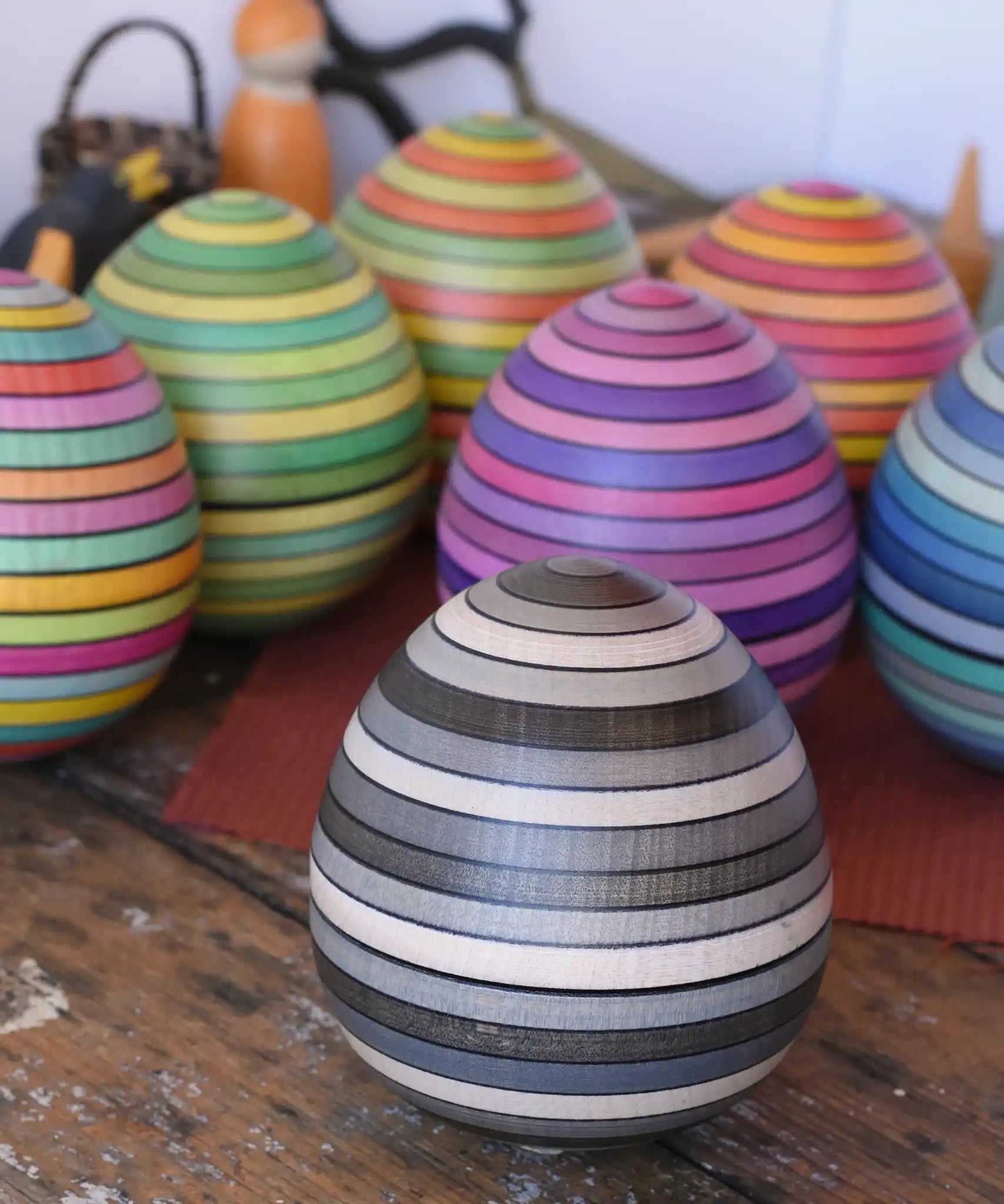 Mader Kreiselmanufaktur roly-poly wooden egg in graphite placed on a wooden surface in the Babipur playroom. Other colour ways of the egg can be seen in the background. 