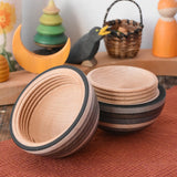 Mader Kreiselmanufaktur roly-poly wooden egg in graphite opened and placed on a wooden surface in the Babipur playroom. The wooden thread can be seen on the sides of the egg.
