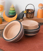 Mader Kreiselmanufaktur roly-poly wooden egg in graphite opened and placed on a wooden surface in the Babipur playroom. The wooden thread can be seen on the sides of the egg.