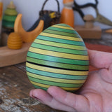 Mader Kreiselmanufaktur roly-poly wooden egg in green in an adult's hand in the Babipur playroom.