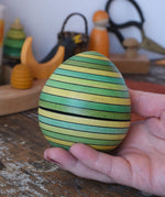 Mader Kreiselmanufaktur roly-poly wooden egg in green in an adult's hand in the Babipur playroom.