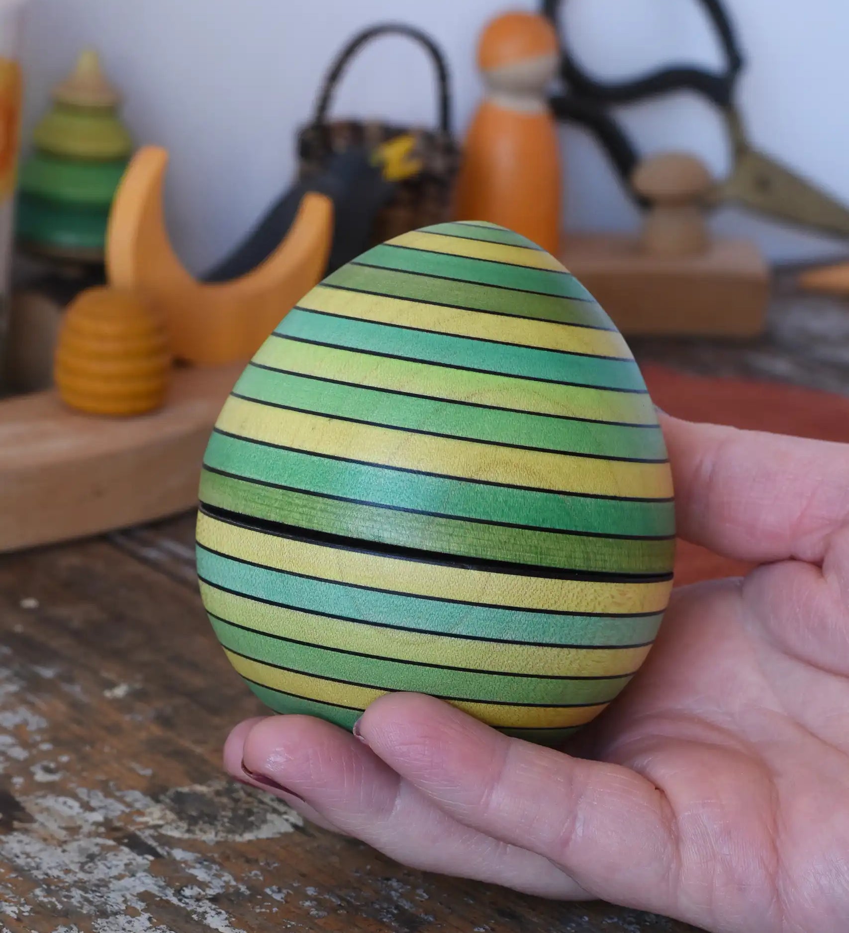 Mader Kreiselmanufaktur roly-poly wooden egg in green in an adult's hand in the Babipur playroom.