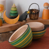 Mader Kreiselmanufaktur roly-poly wooden egg in green opened and placed on a wooden surface in the Babipur playroom. The wooden thread can be seen on the sides of the egg.