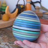 Mader Kreiselmanufaktur roly-poly wooden egg in ice blue in an adult's hand.