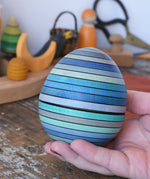 Mader Kreiselmanufaktur roly-poly wooden egg in ice blue in an adult's hand.