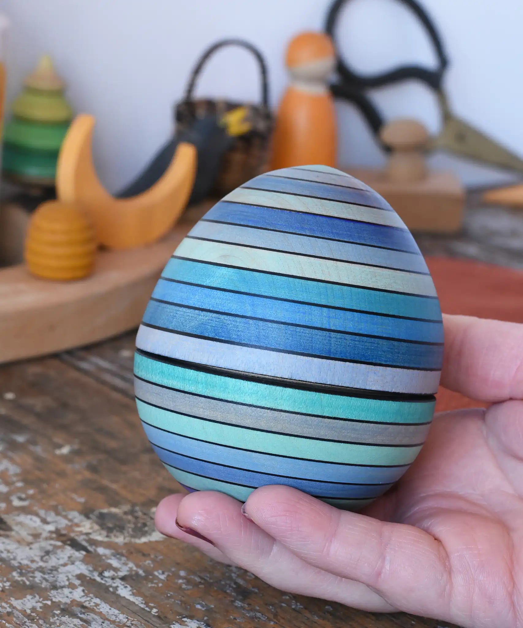 Mader Kreiselmanufaktur roly-poly wooden egg in ice blue in an adult's hand.