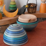 Mader Kreiselmanufaktur roly-poly wooden egg in ice blue opened and placed on a wooden surface in the Babipur playroom. The wooden thread can be seen on the sides of the egg.