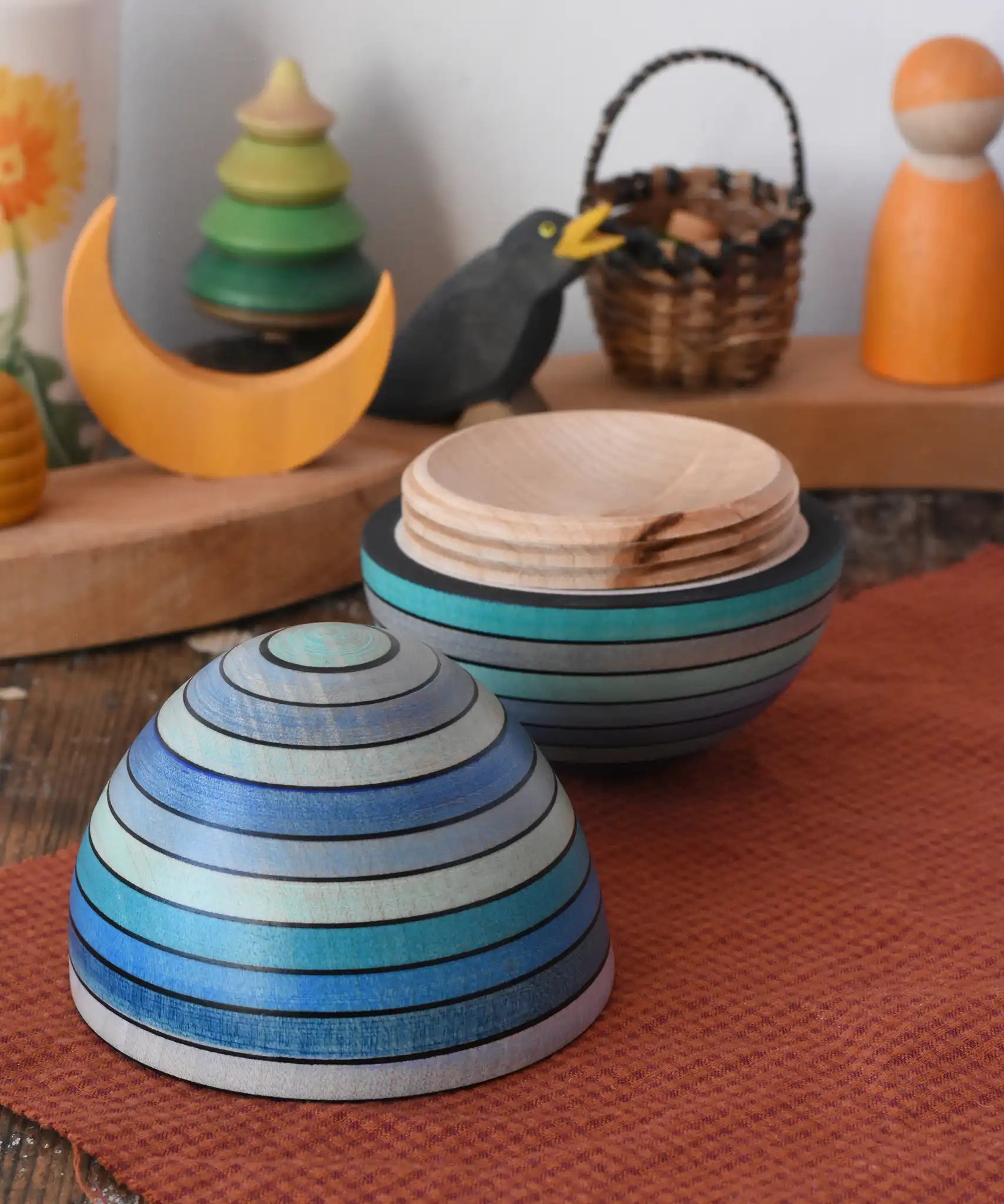 Mader Kreiselmanufaktur roly-poly wooden egg in ice blue opened and placed on a wooden surface in the Babipur playroom. The wooden thread can be seen on the sides of the egg.
