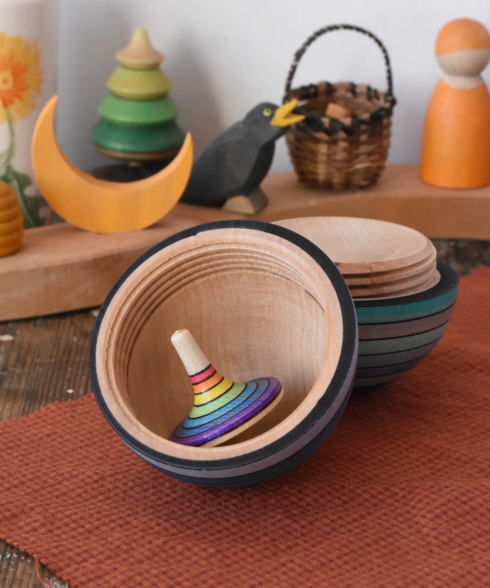 Mader Kreiselmanufaktur roly-poly wooden egg in ice blue stripes opened with a rainbow rallye spinning top placed inside in the Babipur playroom.