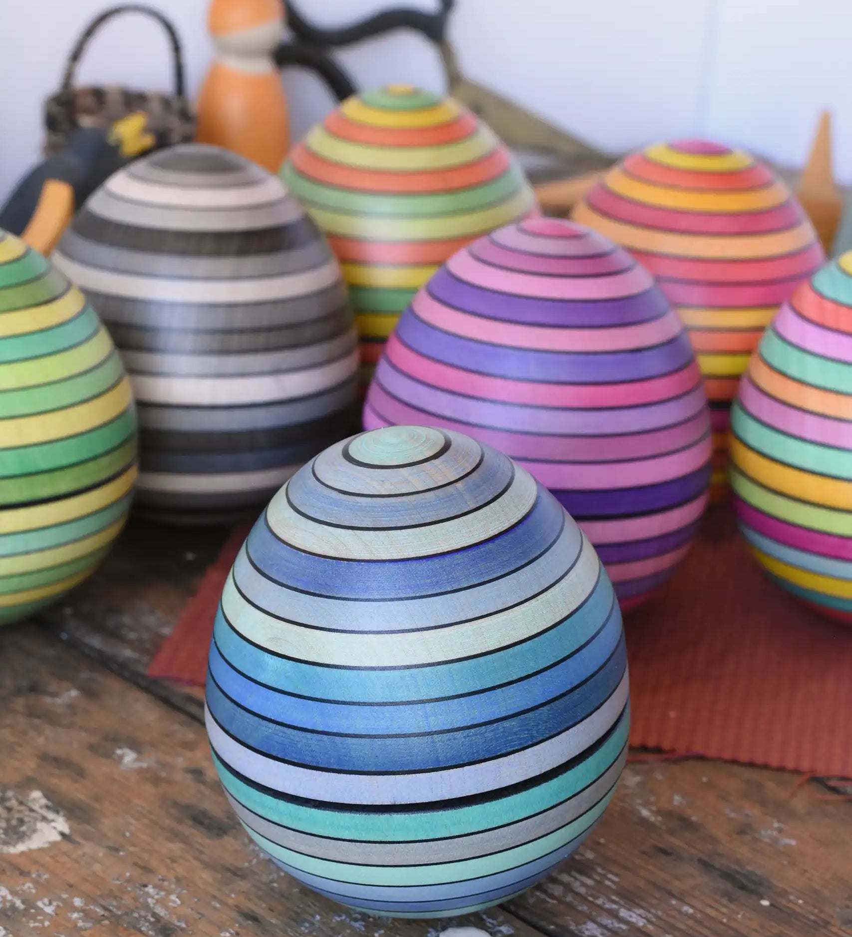 Mader Kreiselmanufaktur roly-poly wooden egg in ice blue placed on a wooden surface in the Babipur playroom. Other colour ways of the egg can be seen in the background.