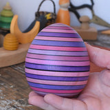 Mader Kreiselmanufaktur roly-poly wooden egg in lilac in an adult's hand in the Babipur playroom.