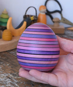 Mader Kreiselmanufaktur roly-poly wooden egg in lilac in an adult's hand in the Babipur playroom.
