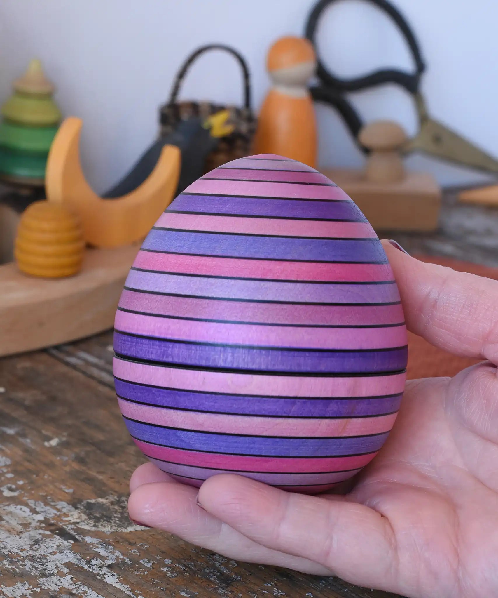 Mader Kreiselmanufaktur roly-poly wooden egg in lilac in an adult's hand in the Babipur playroom.