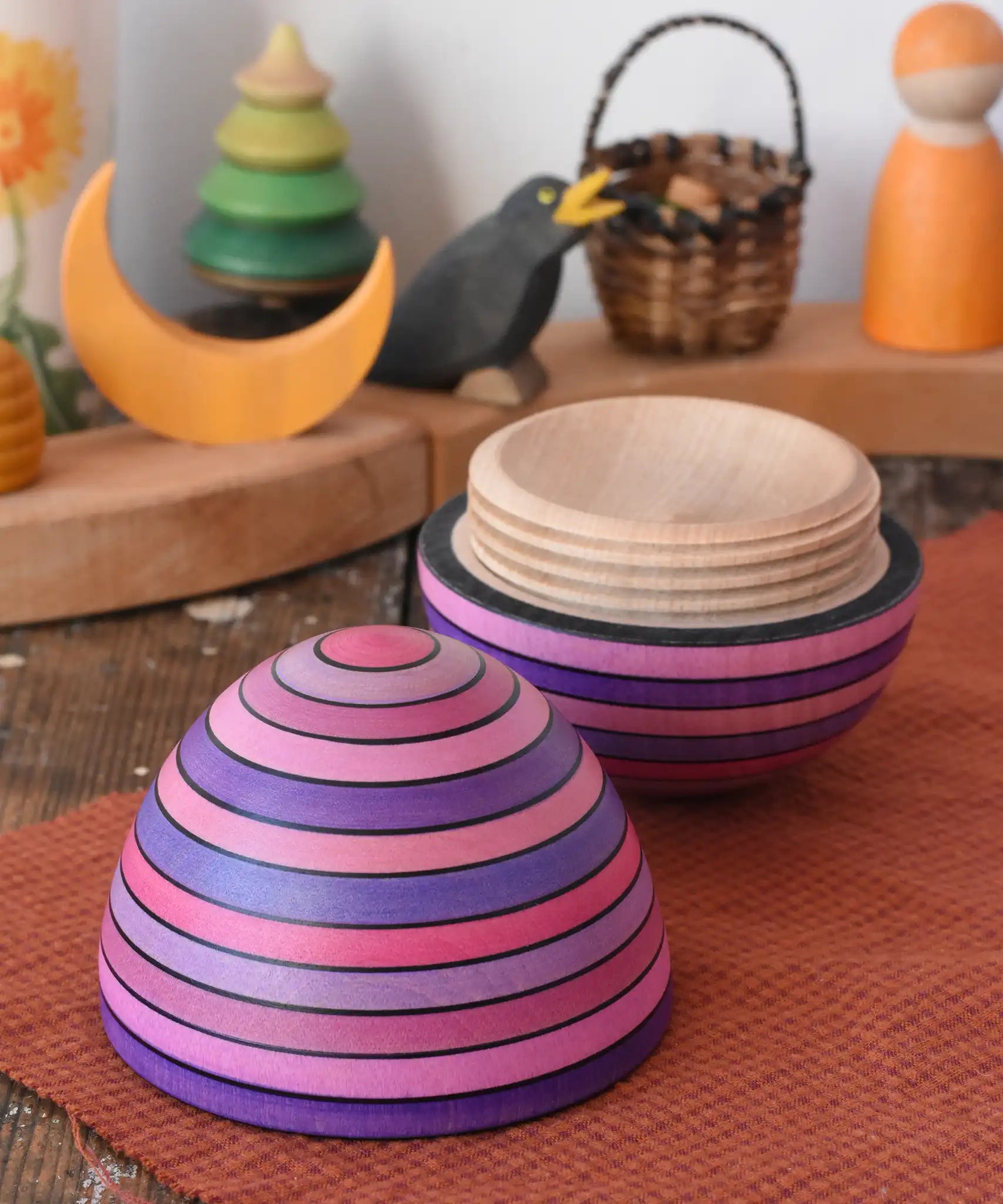 Mader Kreiselmanufaktur roly-poly wooden egg in lilac opened and placed on a wooden surface in the Babipur playroom. The wooden thread can be seen on the sides of the egg.