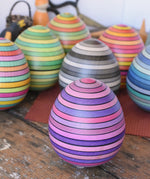 Mader Kreiselmanufaktur roly-poly wooden egg in lilac placed on a wooden surface in the Babipur playroom. Other colour ways of the egg can be seen in the background.