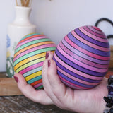 Two Mader Kreiselmanufaktur roly-poly wooden egg in lilac and spring colours in an adult's hand in the Babipur playroom.