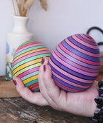 Two Mader Kreiselmanufaktur roly-poly wooden egg in lilac and spring colours in an adult's hand in the Babipur playroom.