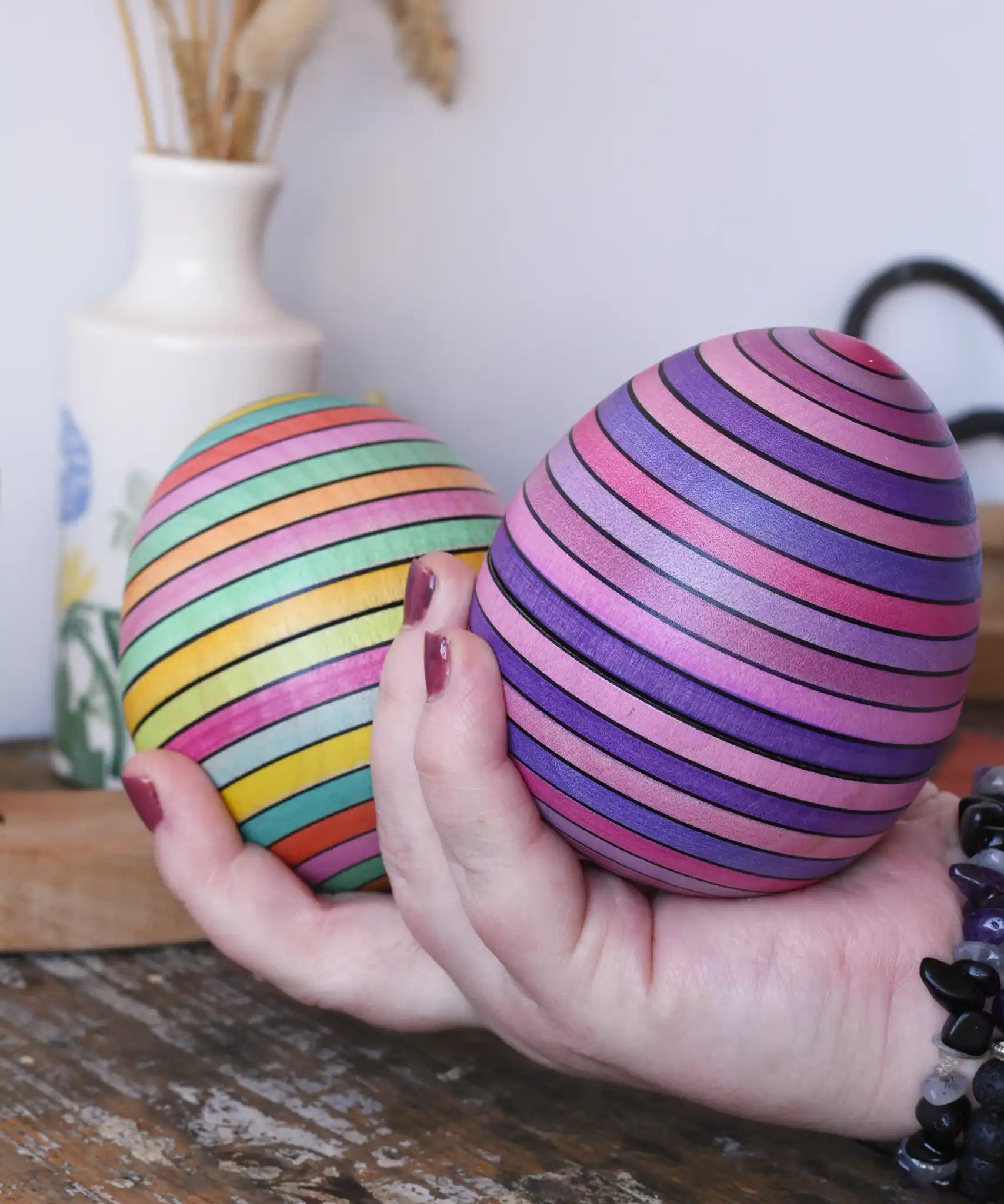 Two Mader Kreiselmanufaktur roly-poly wooden egg in lilac and spring colours in an adult's hand in the Babipur playroom.