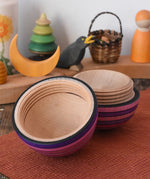 Mader Kreiselmanufaktur roly-poly wooden egg in lilac opened and placed on a wooden surface in the Babipur playroom. The wooden thread can be seen on the sides of the egg.