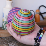 Two Mader Kreiselmanufaktur roly-poly wooden eggs  in spring and lilac in an adult's hand.