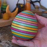 Mader Kreiselmanufaktur roly-poly wooden egg in Spring colour stripe in an adult's hand.