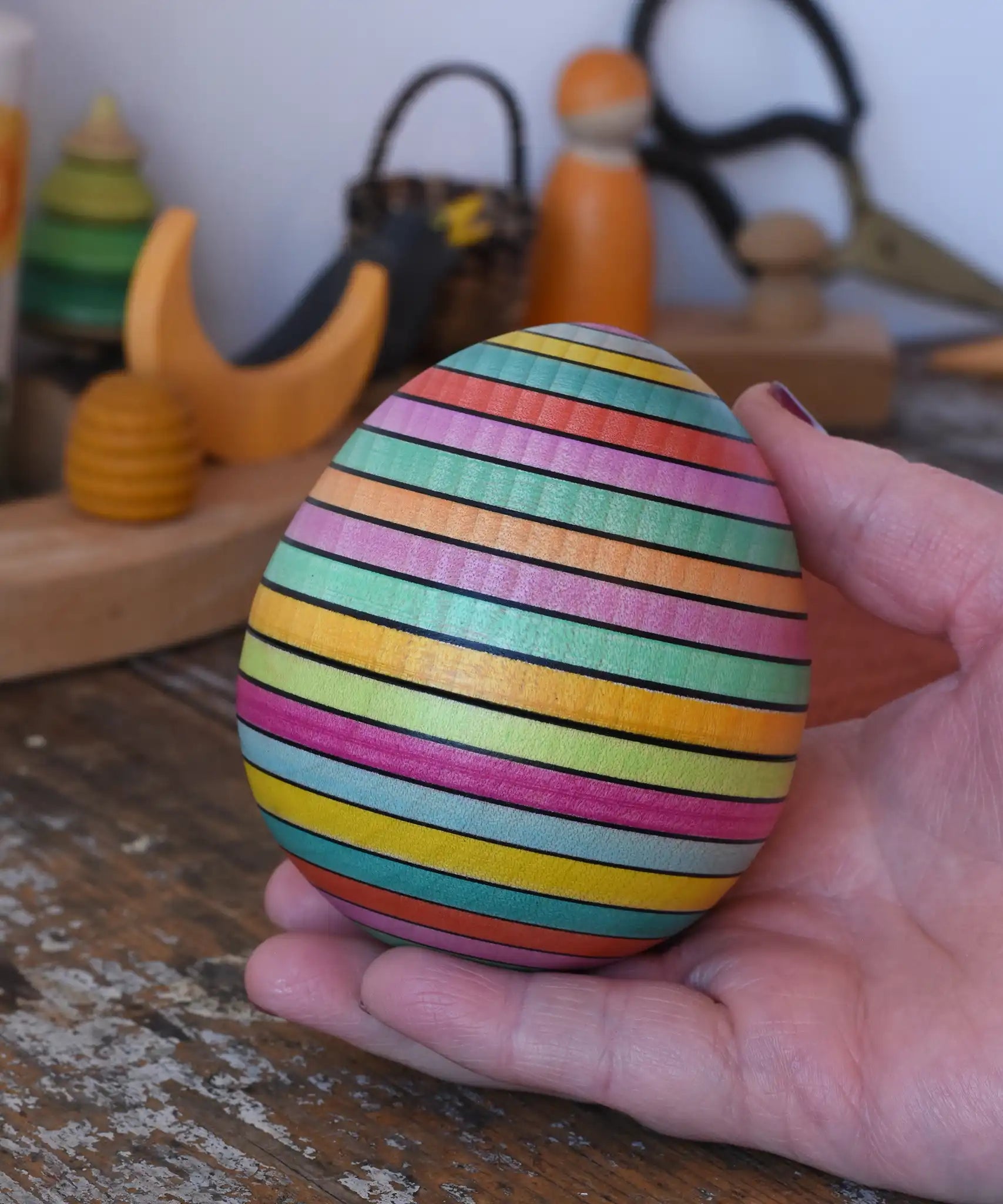 Mader Kreiselmanufaktur roly-poly wooden egg in Spring colour stripe in an adult's hand.
