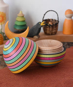 Mader Kreiselmanufaktur roly-poly wooden egg in Spring opened and placed on a wooden surface in the Babipur playroom. The wooden thread can be seen on the sides of the egg.